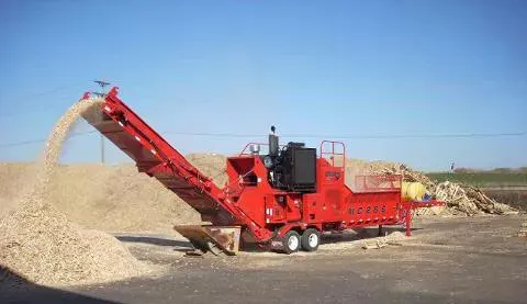 large red wood chipper spitting out mulch into piles