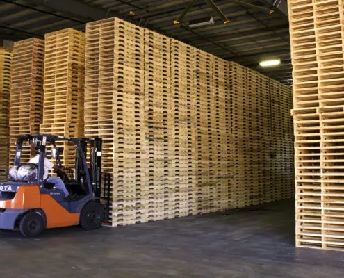 warehouse full of wooden pallets and heavy machinery vehicle picking some up